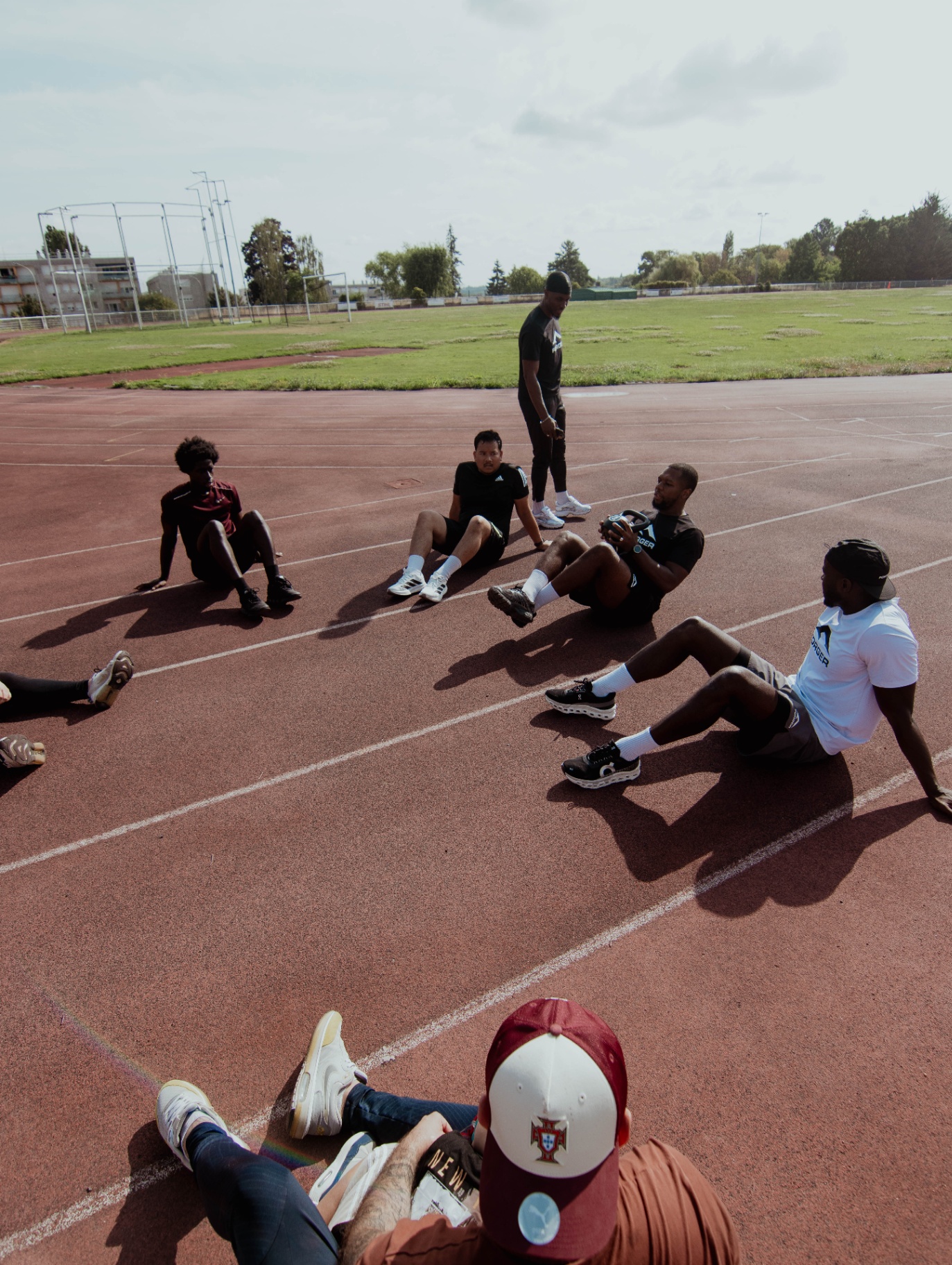Participants du AM BOOTCAMP en cercle sur la piste, exercice au médecine-ball