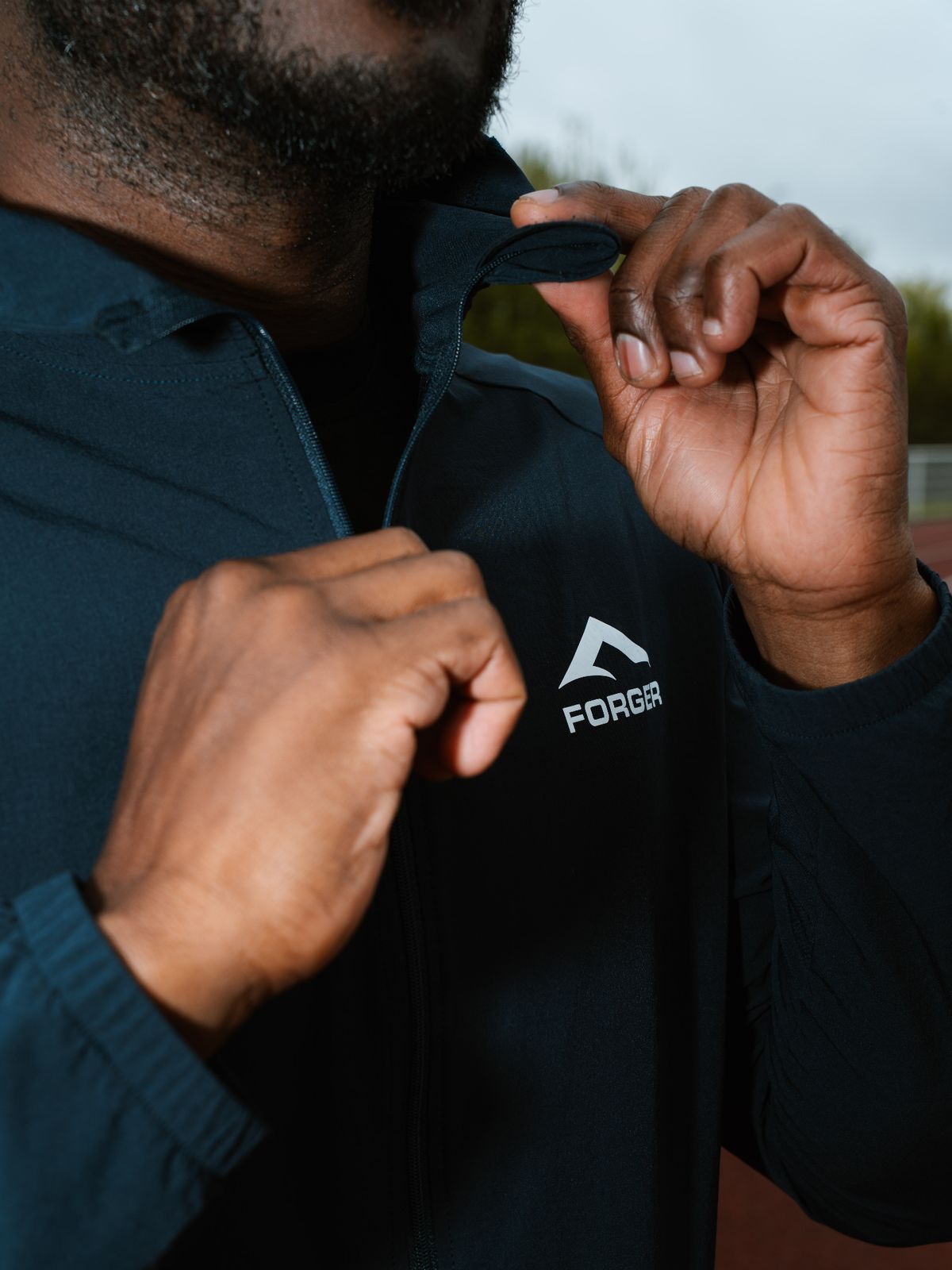 Athlète FORGER ajustant le col de sa veste zippée, logo poitrine.
