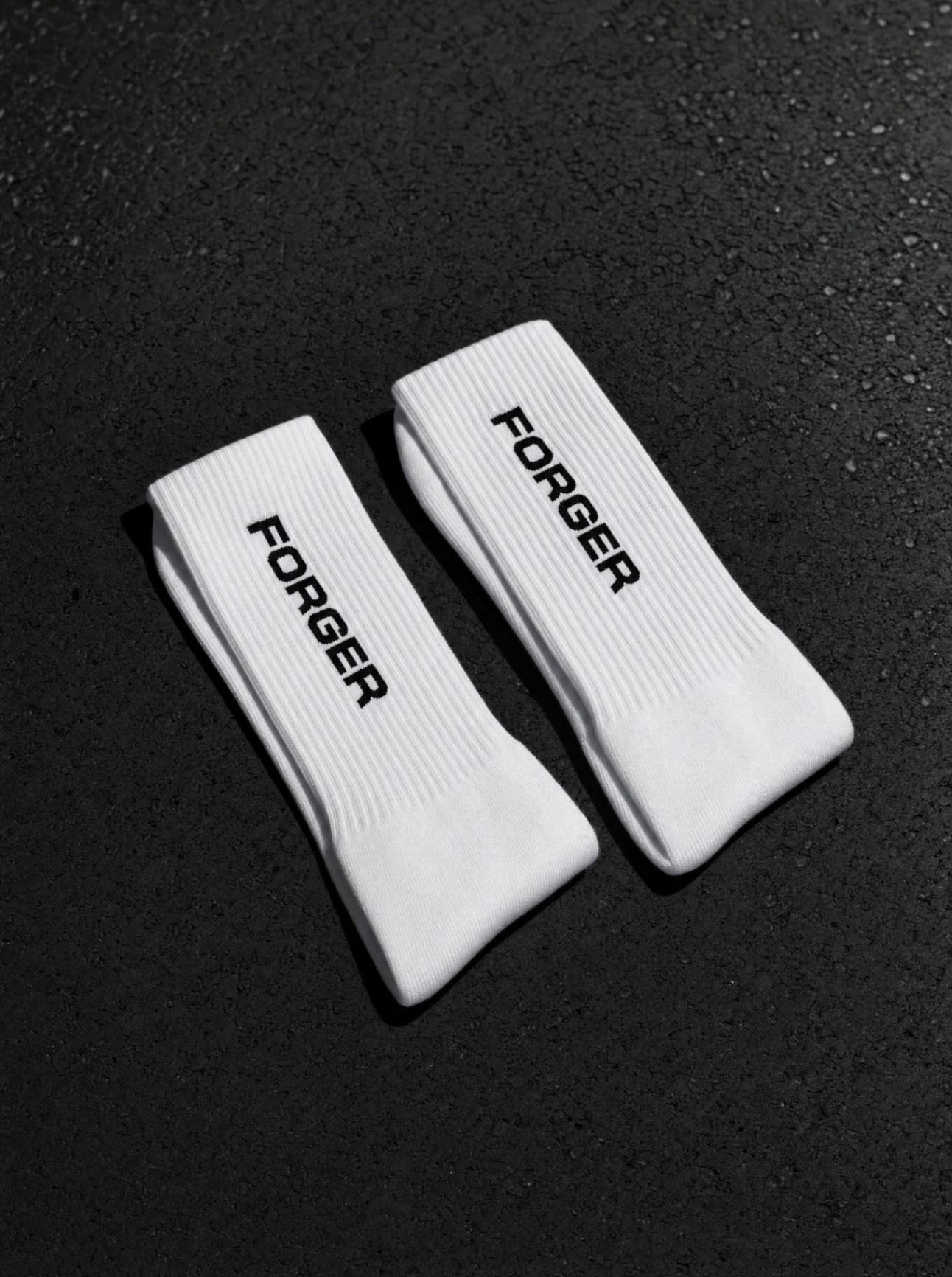 Paire de chaussettes FORGER blanches posées sur asphalte sombre.