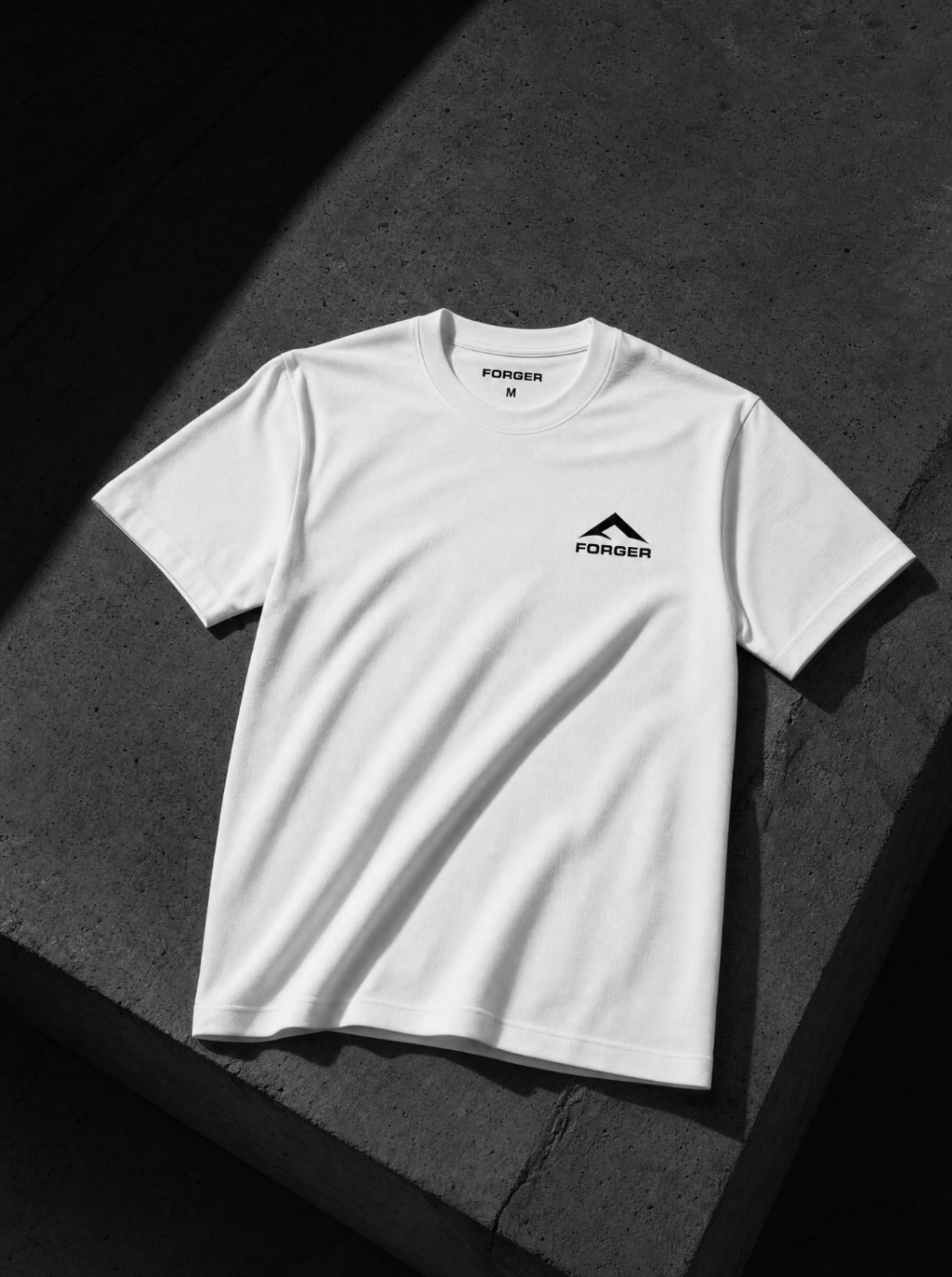 T-shirt FORGER blanc, petit logo poitrine, posé sur béton brut.