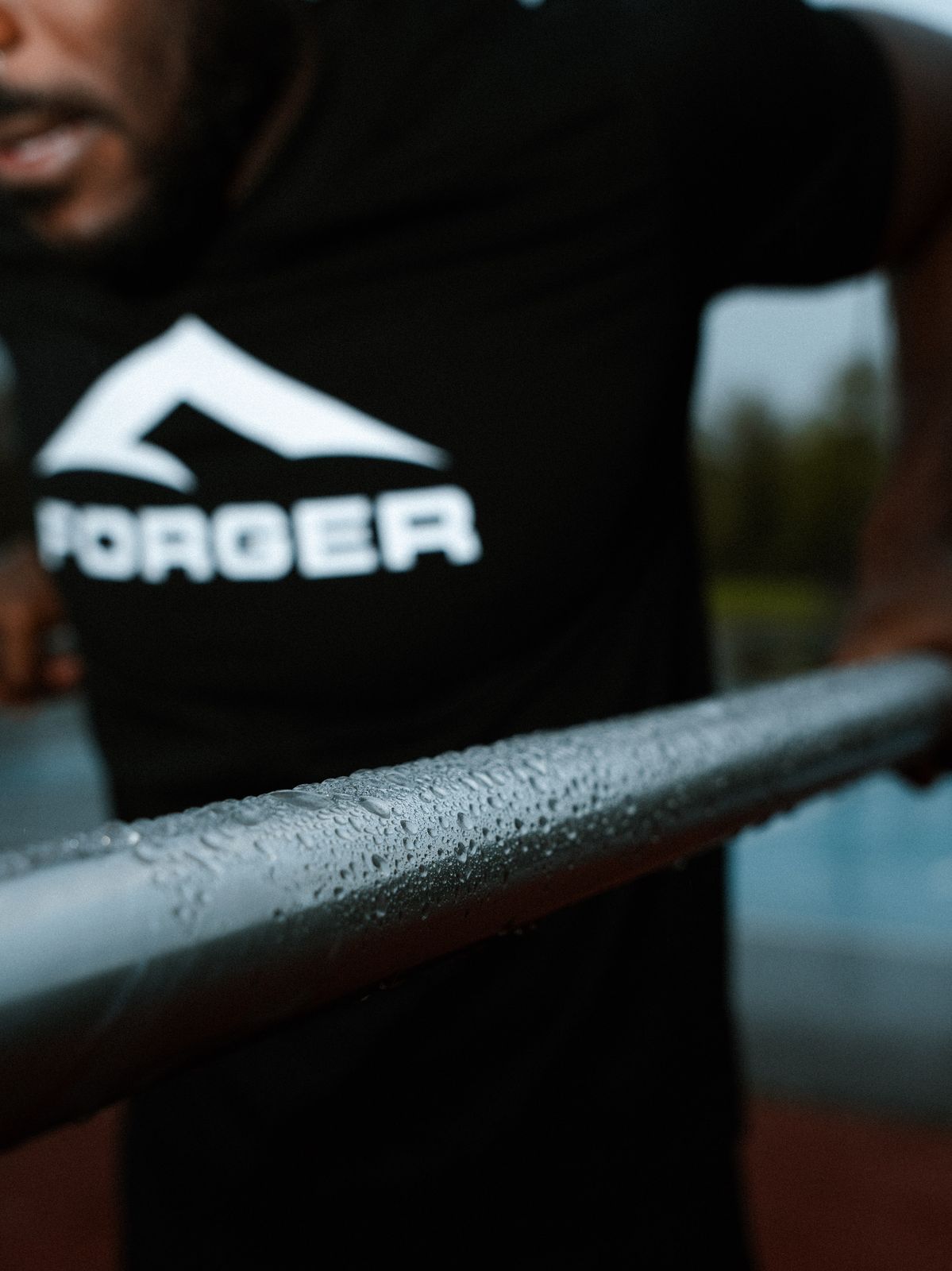 Athlète FORGER en t-shirt logo blanc, barre humide en premier plan.