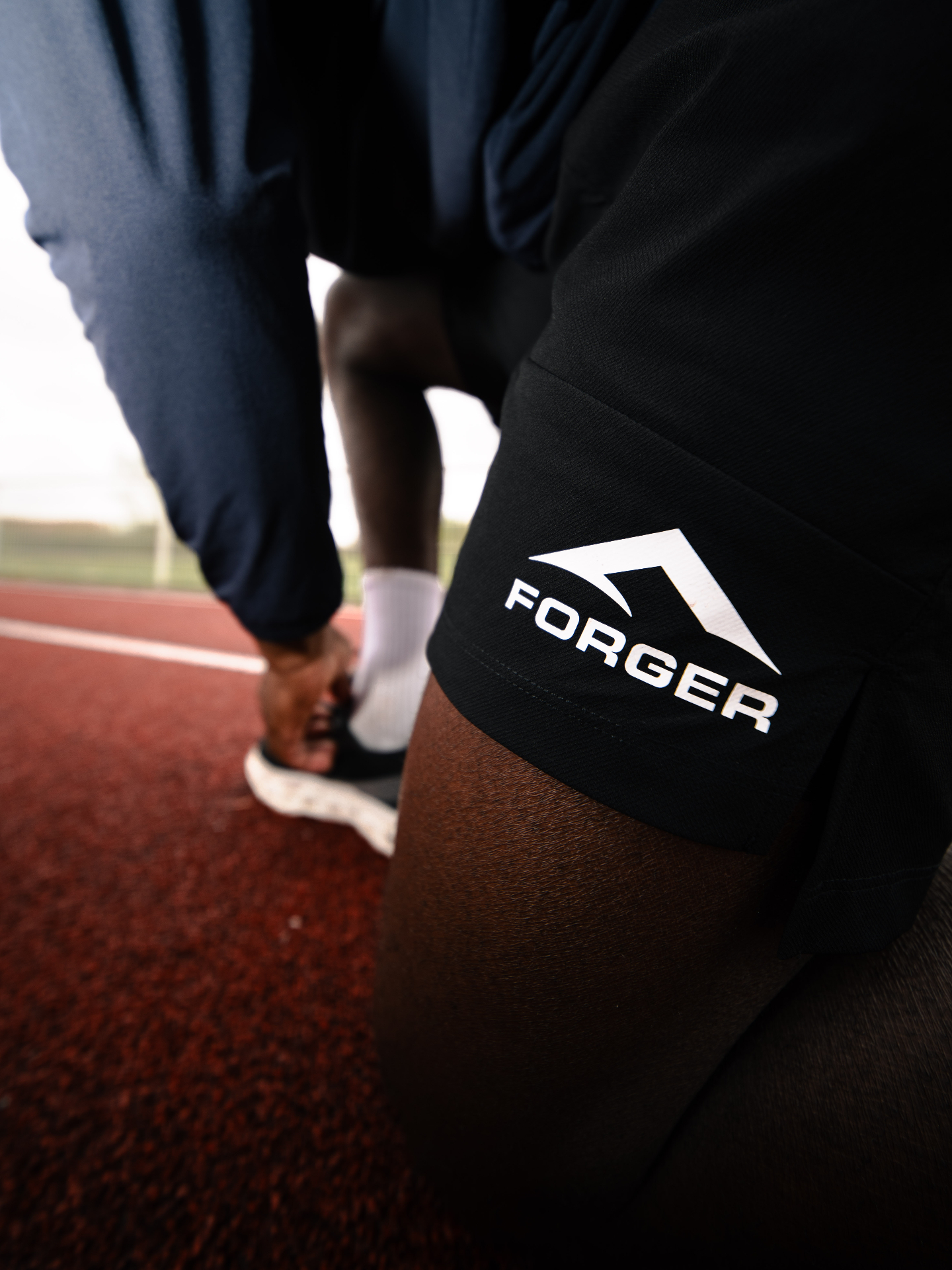 Short FORGER noir avec logo blanc, athlète en position de départ sur piste.