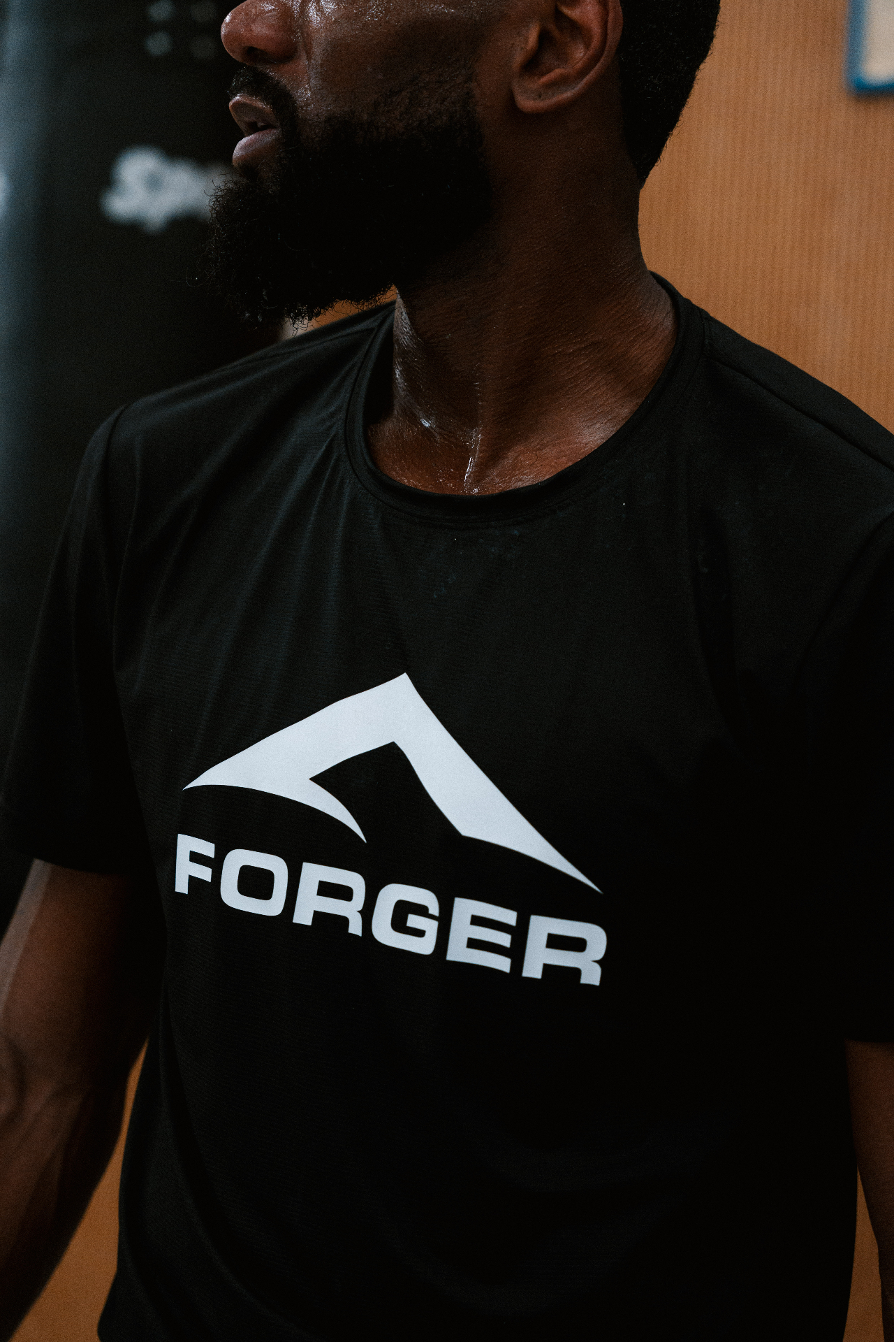 T-shirt FORGER noir avec gros logo central porté par un athlète en salle.