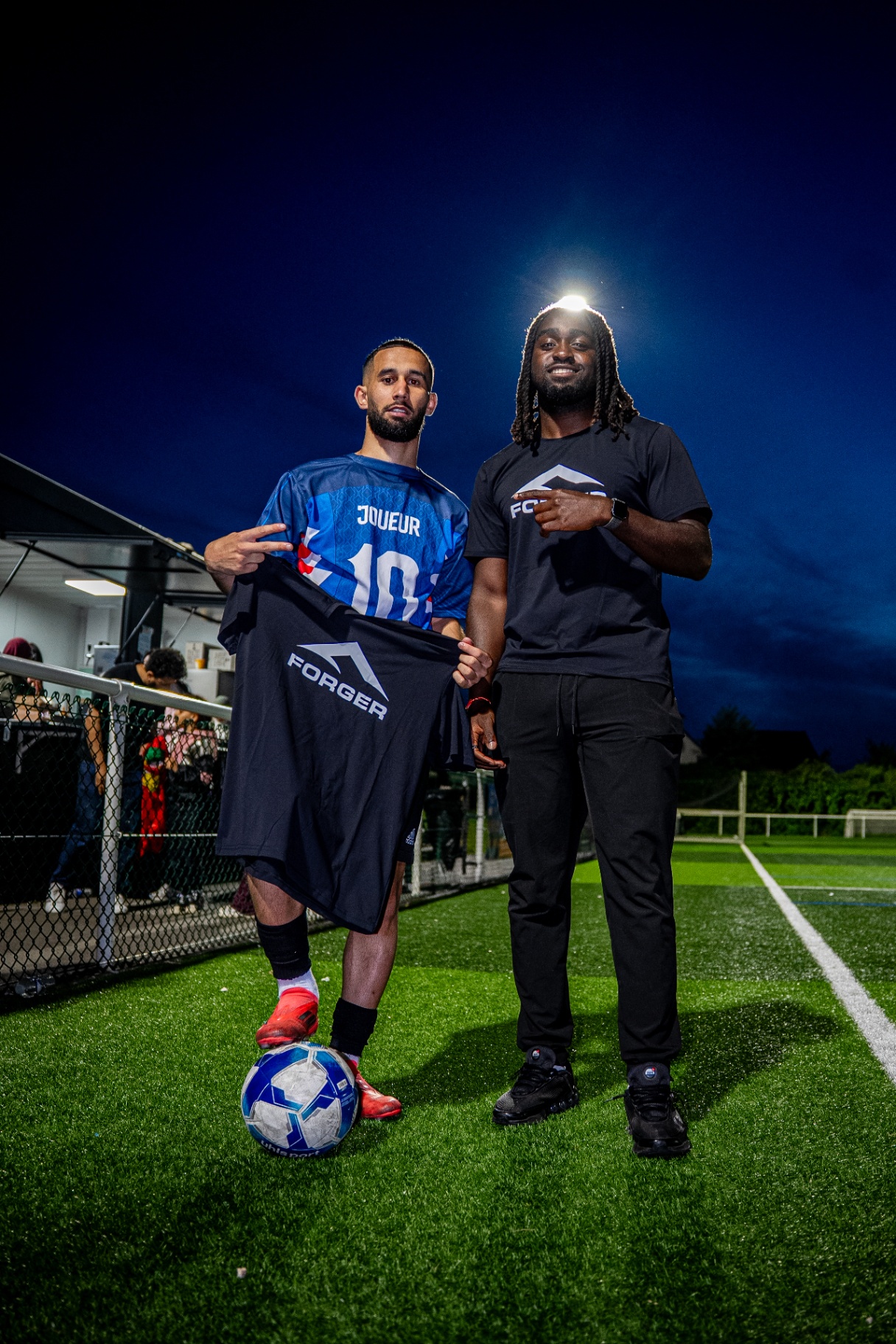 Joueur en maillot bleu numéro 10 tenant un maillot FORGER aux côtés d'un membre de la marque