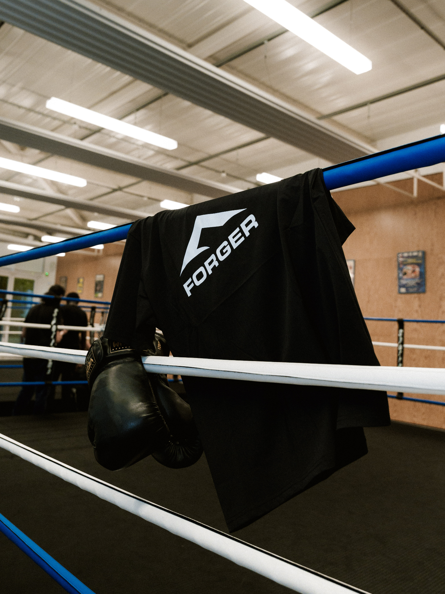 FORGER — t-shirt noir posé sur les cordes d'un ring de boxe avec gants d'entraînement, manifeste discipline et effort